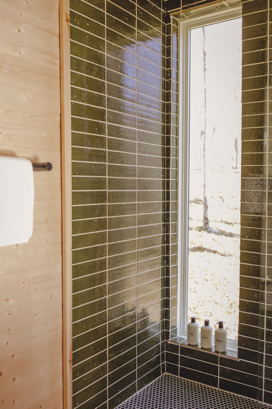 The shower, lined in small green tile, lit from a window above